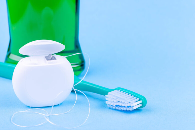Fio dental, escova de dentes e enxaguatório bucal em fundo azul. Produtos para cuidados dentários e higiene bucal