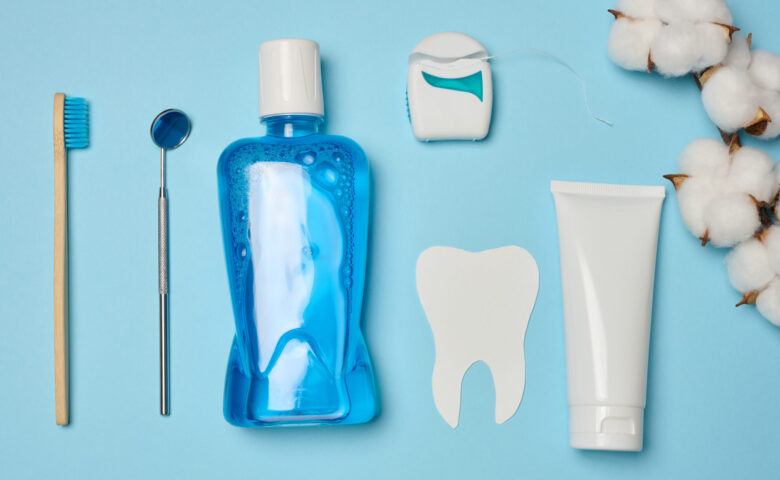 Enxaguatório bucal, tubo de pasta de dente, fio dental e espelho médico em um fundo azul